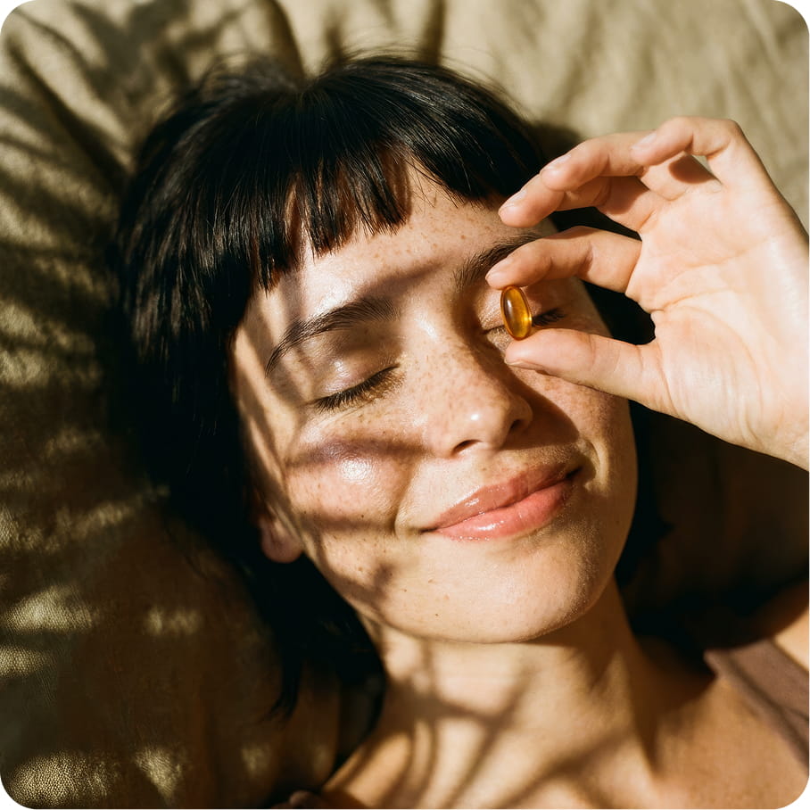 Woman holding a daily softgel in warm sunlight